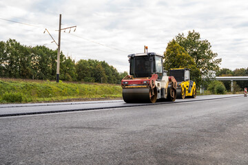 Road rollers compacting new asphalt layer during road construction on countryside highway