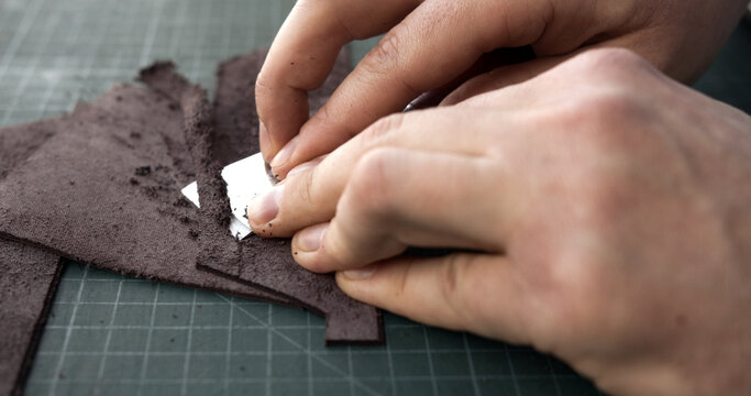 Artisan preparing brown leather edges for gluing in handmade leather crafting process
