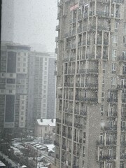 Snowfall over tall residential buildings and parked cars in the city. Used in architecture, climate, and urban environment materials.