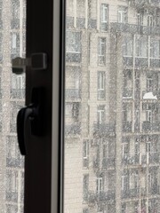 Snow falling outside a closed window with a view of an apartment building. Used in architecture, climate, and urban environment materials.