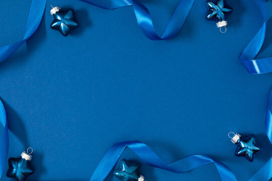Blue ribbon and star-shaped Christmas ornaments on blue background. Minimalist festive composition with copy space. Elegant winter layout for greeting cards and holiday design