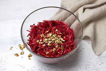 Healthy beetroot salad with shredded carrot, celery, onion, and chopped walnuts in a glass bowl on light textured background. Fresh vegetarian dish, close-up, with copy space for text or design