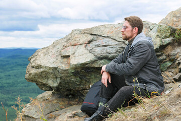 Man in a gray jacket is sitting on a mountain top.