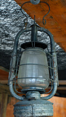 Close-up of an old metal oil lantern with glass shade, hanging in a rustic wooden cabin, evoking nostalgia and vintage charm
