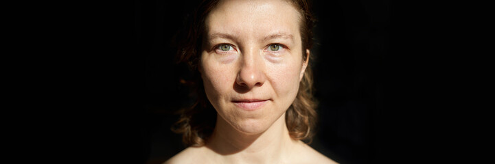 Fototapeta premium Caucasian female adult with light brown hair in natural lighting with black background.