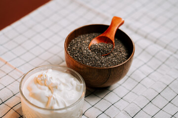 Roasted chia seeds in a wooden bowl with yogurt and wooden spoon on a checkered cloth