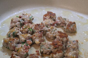 Uncased sausage meat mixed with herbs and spices, seared and sizzling in frying pan.