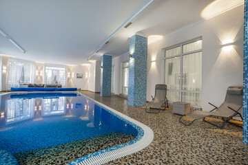 A serene indoor swimming pool features smooth blue water surrounded by elegant tiles. Comforting loungers invite guests to relax in a peaceful atmosphere during the evening.