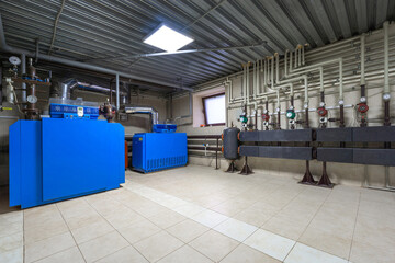 In a well-lit industrial boiler room, blue machinery and a network of pipes create an organized...
