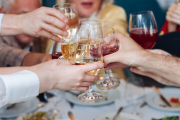 Group of guests celebrate and raise glasses, toasting and cheering with alcohol glasses with wine and champagne in the restaurant on corporate christmas birthday party event or wedding celebration