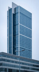 Fototapeta premium Modern glass skyscraper with geometric design against a cloudy sky