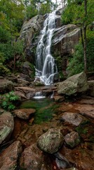 Cascading waterfall flowing over granite rocks into clear pool, surrounded by trees