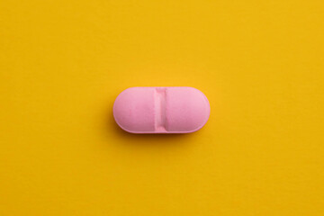 Single, pink, oblong pill on yellow background.