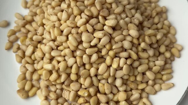 Peeled pine nuts are poured into a wooden bowl in slow motion. Pine nut kernels close up. Healthy nut