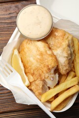 British Traditional Fish and chips with lemon and sauce on wooden table, top view