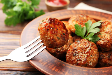 Taking roasted meat patty with fork at wooden table, closeup