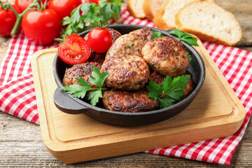 Delicious patties with parsley and tomatoes in pan on wooden table, closeup