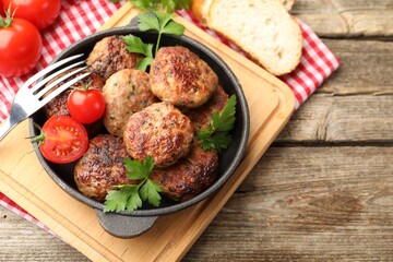Delicious patties with parsley, tomatoes in pan and fork on wooden table, closeup. Space for text