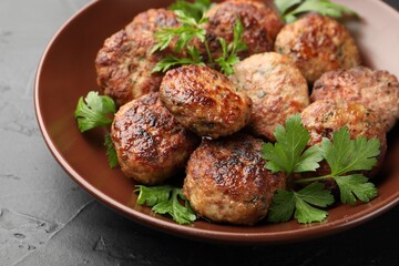 Delicious patties with parsley in bowl on dark textured table, closeup