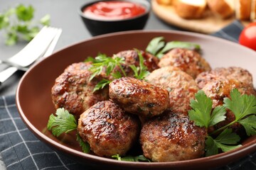 Delicious patties with parsley in bowl on grey table, closeup