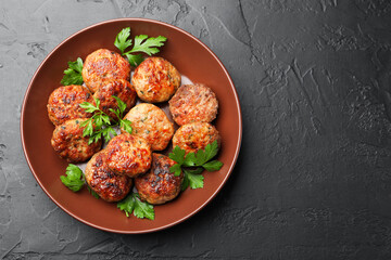 Delicious patties with parsley in bowl on dark textured table, top view. Space for text