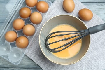 Beaten eggs in bowl and whisk on wooden table, flat lay