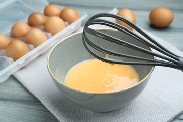 Beaten eggs in bowl and whisk on table, closeup
