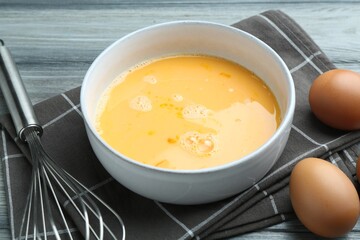 Beaten eggs in bowl and whisk on wooden table, closeup
