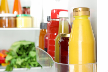 Bottles with different tasty sauces and products in fridge, closeup