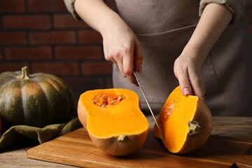 Woman cutting pumpkin at wooden table against brick wall, closeup