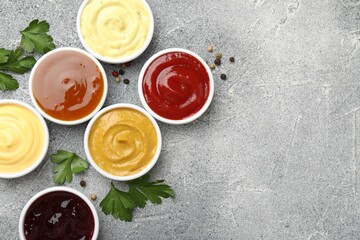 Different tasty sauces in bowls, parsley and peppercorns on grey table, flat lay. Space for text