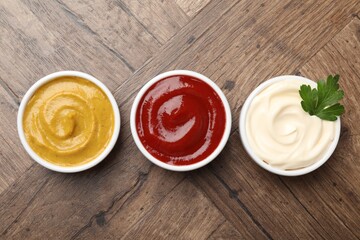 Different tasty sauces in bowls and parsley on wooden table, flat lay