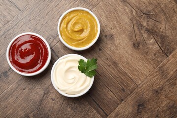 Different tasty sauces in bowls and parsley on wooden table, flat lay. Space for text