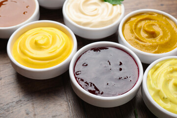Different tasty sauces in bowls on wooden table, closeup