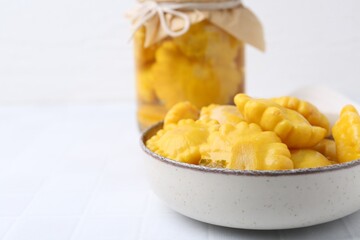 Pickled pattypan squashes in bowl and jar on white tiled table, closeup. Space for text