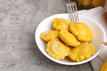 Pickled pattypan squashes in bowl and fork on grey textured table, closeup. Space for text