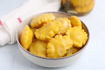 Pickled pattypan squashes in bowl on white tiled table, closeup
