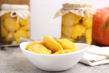 Pickled pattypan squashes in bowl and fork on grey textured table against white background, closeup