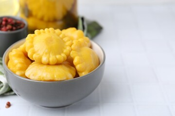 Pickled pattypan squashes in bowl on white tiled table, closeup. Space for text