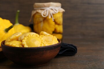 Pickled pattypan squashes in bowl on wooden table, closeup. Space for text
