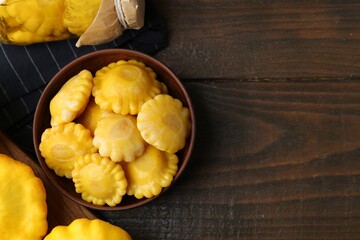 Pickled pattypan squashes in bowl and jar on wooden table, flat lay. Space for text