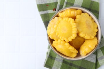 Pickled pattypan squashes in bowl and towel on white tiled table, top view. Space for text
