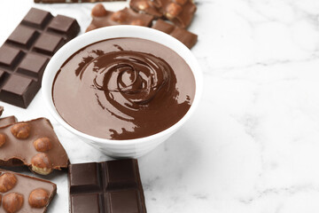 Bowl with melted chocolate and pieces on white marble table, closeup. Space for text