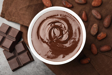 Bowl with melted chocolate, beans and pieces on grey table, flat lay