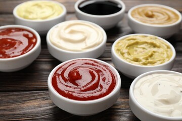 Different sauces in bowls on wooden table, closeup