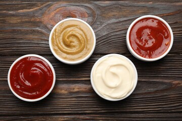 Different sauces in bowls on wooden table, flat lay