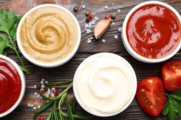 Different sauces, spices and herbs on wooden table, flat lay