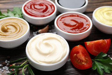 Different sauces, spices and herbs on wooden table, closeup