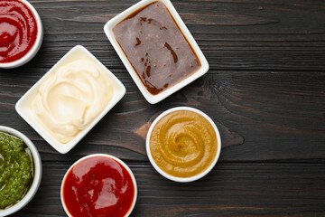 Different sauces in bowls on wooden table, flat lay