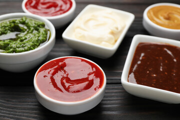Different sauces in bowls on wooden table, closeup